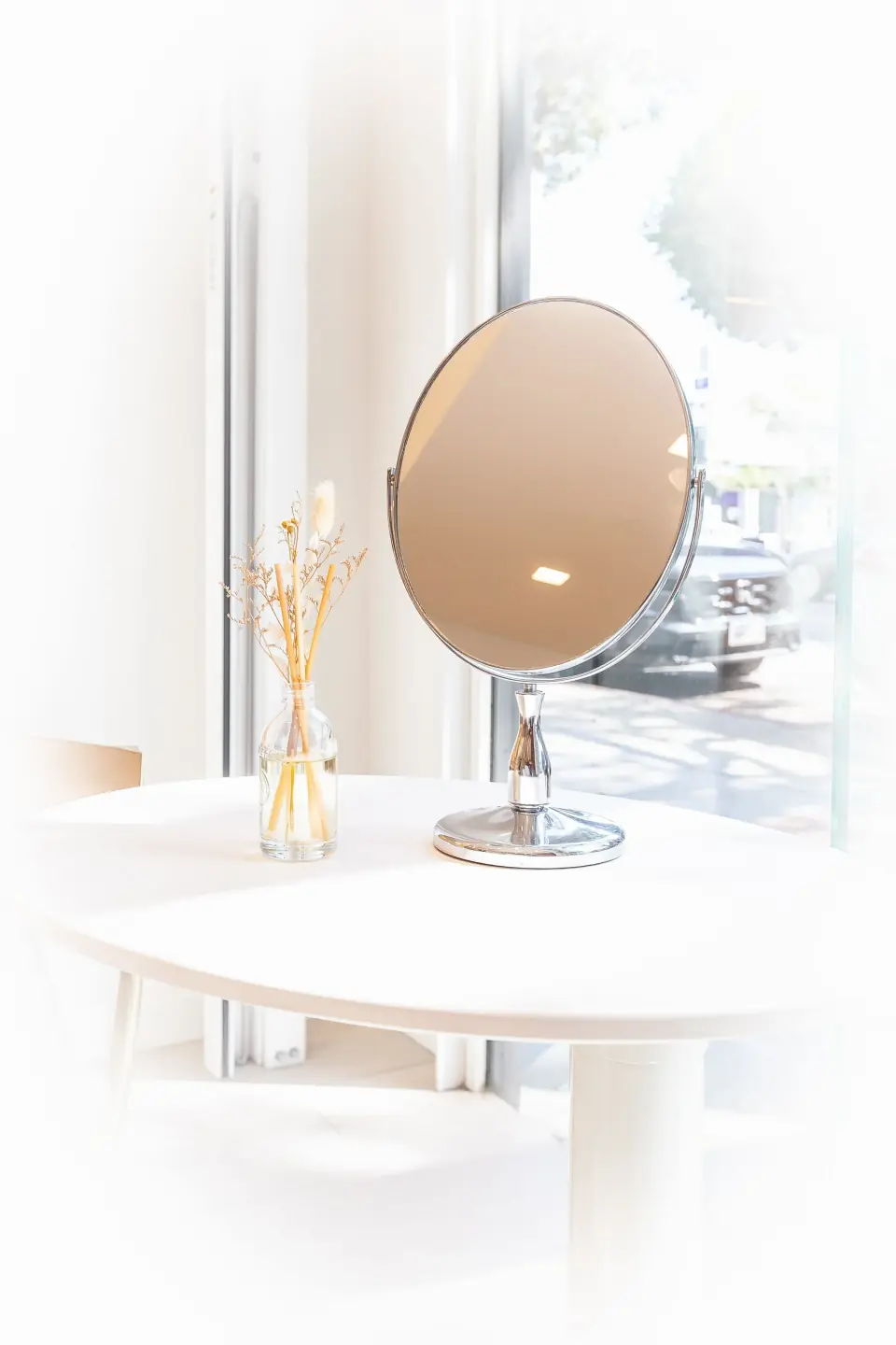 A fitting mirror on a white table by the window